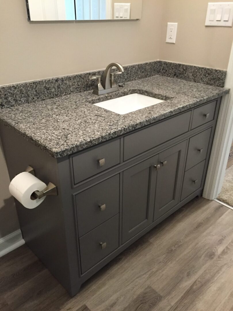 A sink with gray top and cupboards with wooden floors