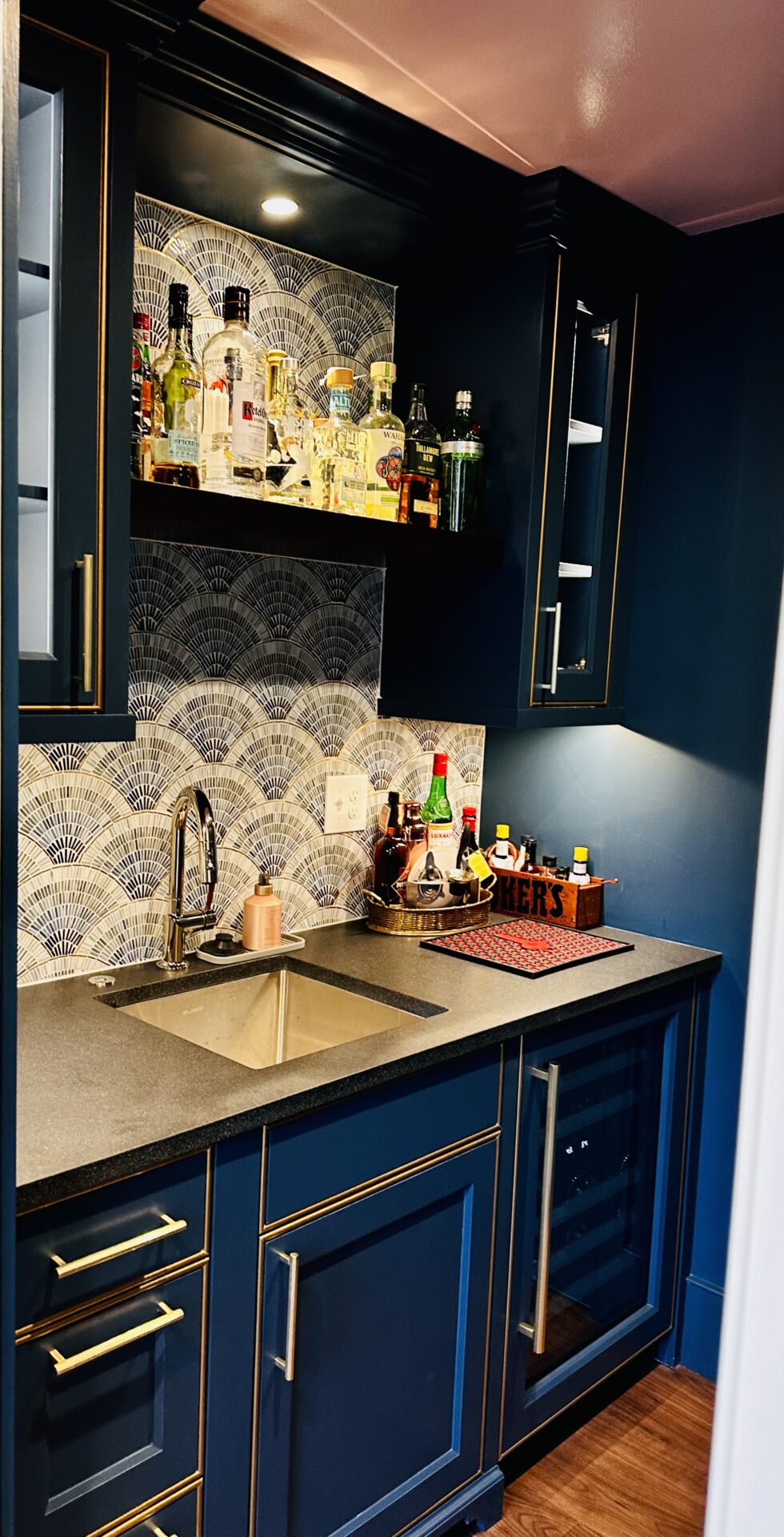 A kitchen with blue cabinets and a sink with bottles in the above shelf